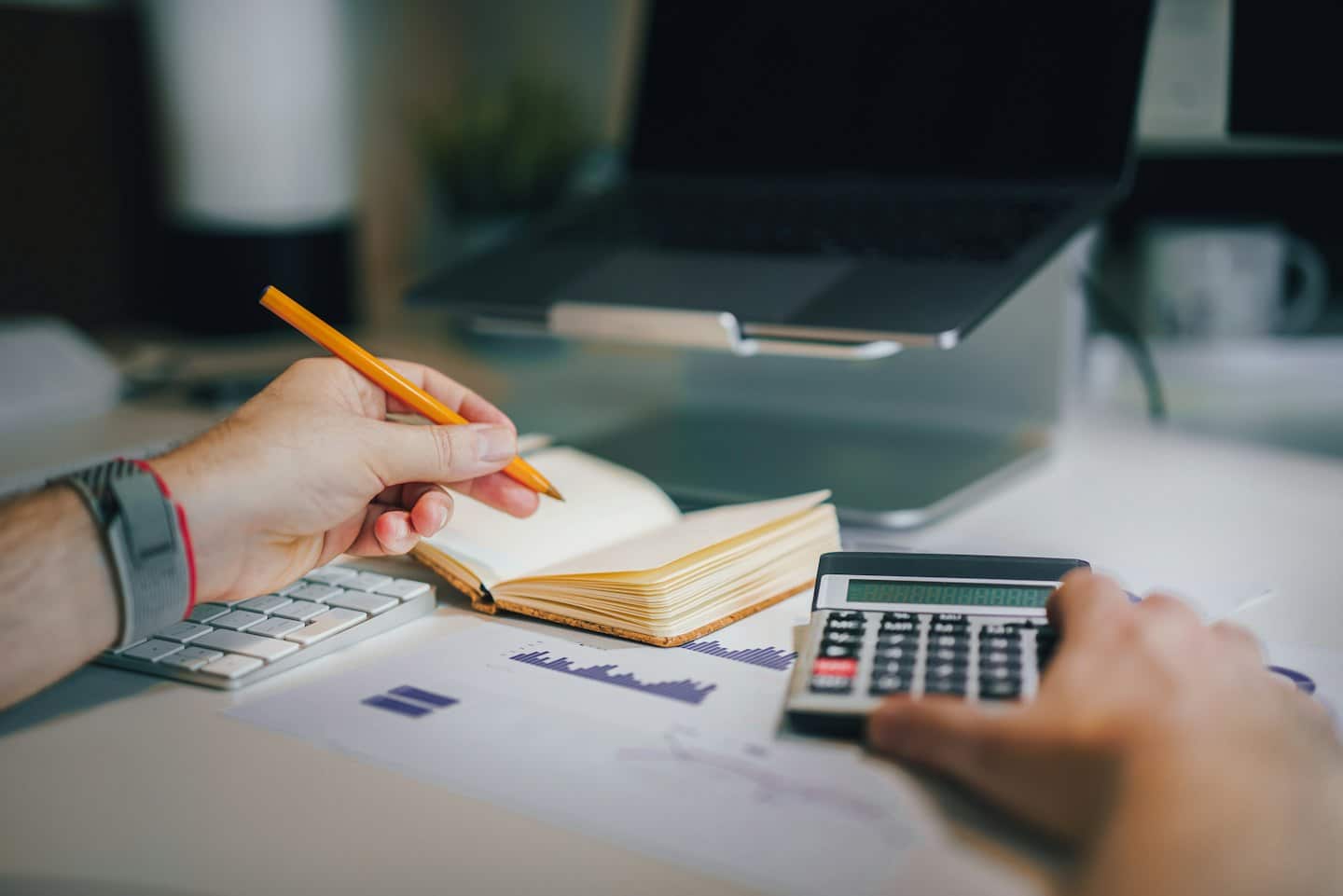 Hands working on a calculator and notebook at a desk.